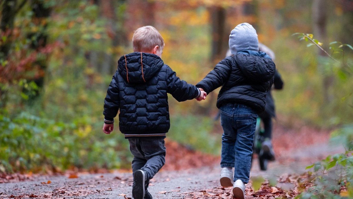 Two children in winter coats running down a trail.